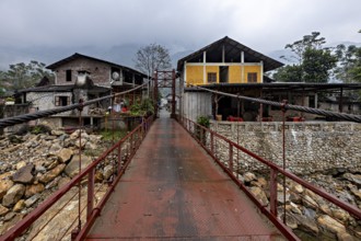 A metal bridge connects two older buildings, one of them yellow, under a grey cloudy sky, A bridge
