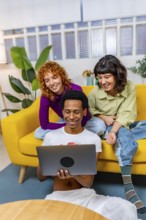 Vertical photo of three multiracial Lgtb people using laptop sitting together in a modern sofa