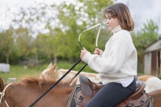 A young girl wearing a sweater rides a horse on a farm, enjoying a peaceful day outdoors. The
