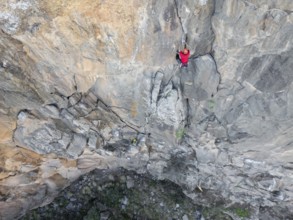Two climbers in red gear expertly scales a rugged rock face using traditional climbing techniques.