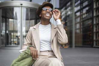 A stylish black woman smiles confidently in an urban setting She wears chic sunglasses and a