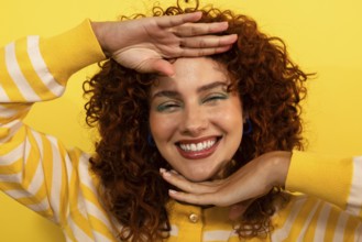 A joyful woman with curly hair looking at camera, smiles brightly against a vivid yellow background