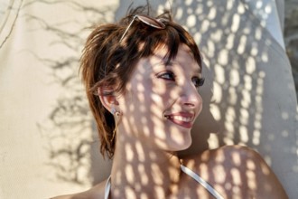 Relaxing at the beach during summer, a young woman lounges on a chair, soaking up the sun. Shadows