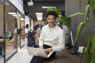 A modern office space features a smiling professional on a laptop, with colleagues interacting in