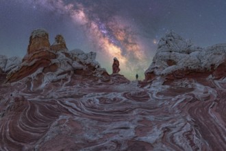 A lone man stands under the Milky Way, gazing at the stars over the unique geological formations of