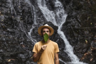 Man from Spain holding a leaf in front of his face, with a waterfall in the Choco Andino