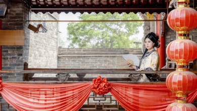 A woman in traditional Qing Dynasty attire, holding a fan, stands gracefully on a decorated balcony