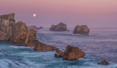 A serene view of rugged sea stacks and cliffs bathed in soft dawn light at Arnia Beach, Costa