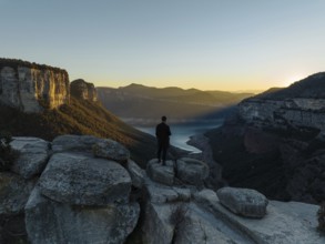 A lone figure stands on rocky cliffs, gazing over the Panta de Sau Reservoir in Catalonia, Spain,