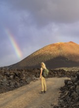 A woman with a backpack stands on a rocky path in Timanfaya National Park, Lanzarote. A vibrant