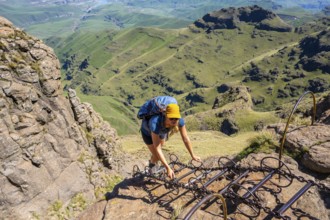 Young female hiker climbs over dangerous ladders, mountains and cliffs of the Drakensberg