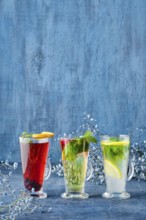 Three glasses with hot fruit and herbal tea on blue background