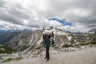 A smiling mother with her baby in a carrier hikes through the breathtaking snow-capped peaks of Tre