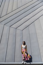 A woman in a vibrant, colorful outfit stands against a backdrop of sleek, modern architecture. Her
