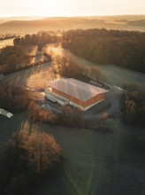 A building surrounded by trees in the warm light of an autumn sunset seen from the air, Gechingen,
