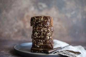 A stack of freshly sliced whole wheat bread with seeds sits artfully arranged on a ceramic plate.