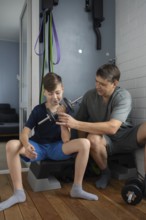 A father helps his young son lift a dumbbell, coaching him on weightlifting techniques in a home