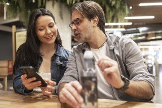 A couple sits at a wooden table, engaged in a lively conversation while sharing something on a