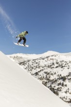 A snowboarder performs an airborne trick over a snow-covered mountain, capturing the essence of