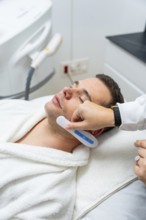 Man receiving modern facial treatment with a handheld device at an aesthetic clinic, focused on