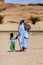 Mother and child, both in traditional dress, walking through a barren desert landscape, woman in