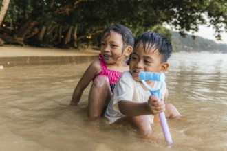 Two cheerful children enjoy playing in the shallow waters of a Philippine beach, with laughter and