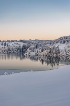 Dawn and sunrise at the wintry Forggensee in a snow-covered winter landscape in the foothills of