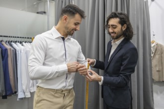 A tailor measures a customer for a custom suit in a suit store. The scene captures precision and