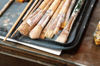 A close-up of well-used paintbrushes with dried paint resting in a fabric case on a wooden table.