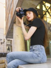 A woman in casual attire takes photos with a professional camera in a city setting. Her focused