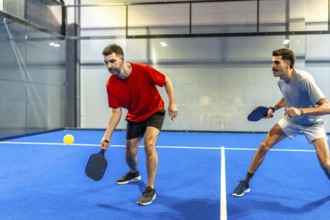 Two male players engaging in an active game of pickleball, holding paddles and focusing on the