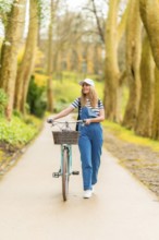 Happy young woman walking with her vintage bicycle in a park, enjoying a sunny day of leisure