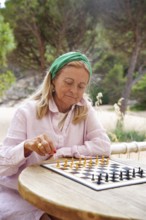 A senior woman plays chess outdoors, deeply focused on her strategic moves The serene natural