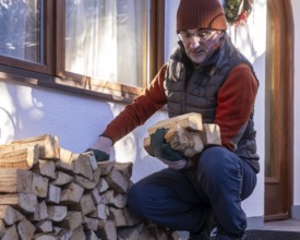 A senior man carefully stacks pieces of eco-friendly firewood outside his home on a sunny day,