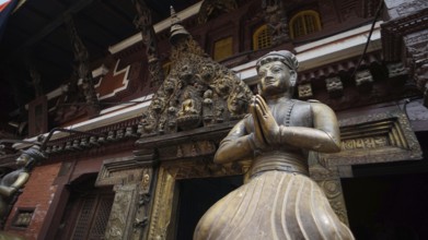 Statue of a praying figure in traditional dress against an ornate temple background, Kathmandu,