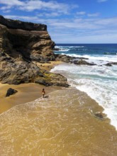 From above drone view of a lone woman walks on the sandy shore of Tindaya Beach in Fuerteventura,