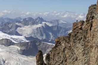 A hiker stands atop a rugged cliff in Zermatt, Switzerland, admiring the panoramic summer view of