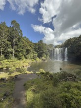 Rainbow Falls waterfall (Waianiwaniwa) amidst lush trees under blue sky with cloudy water,