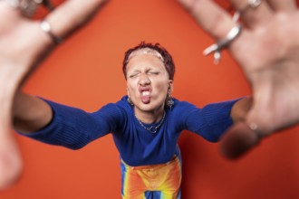 Fashion-forward young woman with vibrant orange background, wearing colorful trousers, tooth gems
