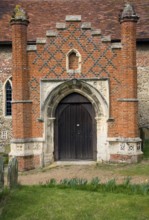 Tudor red brick porch set against more ancient building. St Peter's church, Charsfield Suffolk,