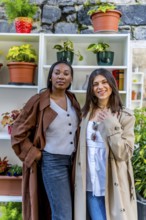 Two young businesswomen wearing stylish trench coats are posing confidently next to a shelf adorned