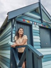 A woman standing on the steps of a colorful Brighton Bathing Box in Melbourne, Australia. The