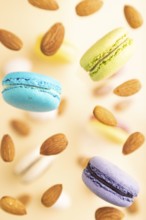 Multicolored flying macaroons and almonds frozen in the air on blurred beige background. top view,