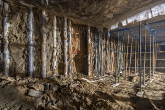 Underground construction site showing exposed dirt walls and temporary supports. The area is dimly