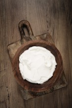 Sour cream in a wooden bowl, on a wooden table, top view, close-up, no people
