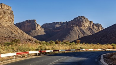 A road with a bend winds its way through impressive mountain scenery in a barren desert landscape