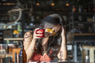 Woman in a cafe, savoring coffee with yellow sunglasses and earphones, enjoying music on a sunny