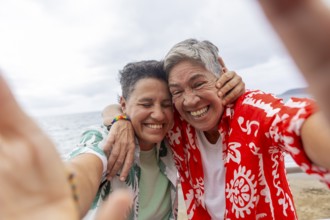 A joyful lesbian couple takes a selfie on a cloudy beach day, showcasing their love and excitement