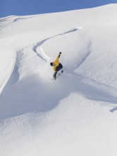 A snowboarder in a yellow jacket executes a jump on a snowy mountain slope. The clear blue sky and