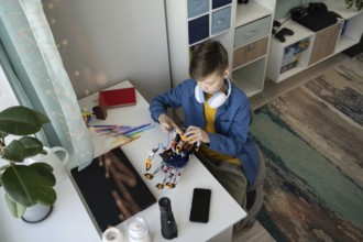 A young boy sits at a white desk, focused on assembling a robot. Surrounded by colorful tools,